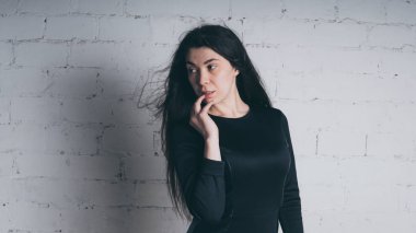 Kız beyaz duvara karşı poz. Siyah elbise modeli. Esmer Doğu görünüyor.