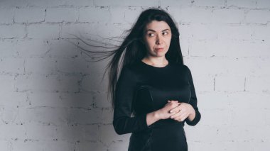 Kız beyaz duvara karşı poz. Siyah elbise modeli. Esmer Doğu görünüyor.