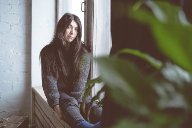 Pencerede, bir öğrenci bir gri süveterli oturan kız. Model pencereye poz. Konsept: romantizm ve özlem