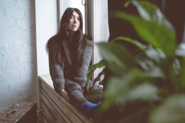 Pencerede, bir öğrenci bir gri süveterli oturan kız. Model pencereye poz. Konsept: romantizm ve özlem