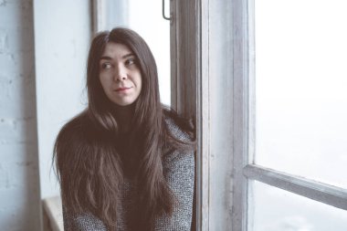 Pencerede, bir öğrenci bir gri süveterli oturan kız. Model pencereye poz. Konsept: romantizm ve özlem