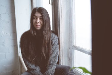 Pencerede, bir öğrenci bir gri süveterli oturan kız. Model pencereye poz. Konsept: romantizm ve özlem