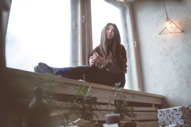 Pencerede, bir öğrenci bir gri süveterli oturan kız. Model pencereye poz. Konsept: romantizm ve özlem