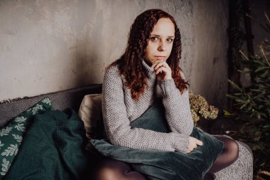 Bir genç kız yatakta oturmuş bir kazaklı bir battaniyeye huddled. Sıcak kazak giymiş kadın sokak stil giyim. Temiz cilt, uzun saç