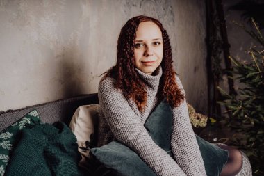 Bir genç kız yatakta oturmuş bir kazaklı bir battaniyeye huddled. Sıcak kazak giymiş kadın sokak stil giyim. Temiz cilt, uzun saç