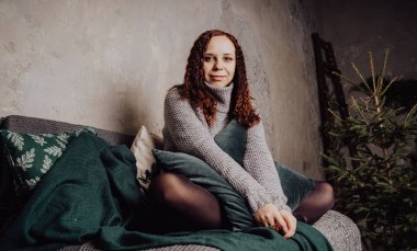 Bir genç kız yatakta oturmuş bir kazaklı bir battaniyeye huddled. Sıcak kazak giymiş kadın sokak stil giyim. Temiz cilt, uzun saç