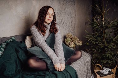 Bir genç kız yatakta oturmuş bir kazaklı bir battaniyeye huddled. Sıcak kazak giymiş kadın sokak stil giyim. Temiz cilt, uzun saç