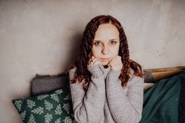 Bir genç kız yatakta oturmuş bir kazaklı bir battaniyeye huddled. Sıcak kazak giymiş kadın sokak stil giyim. Temiz cilt, uzun saç