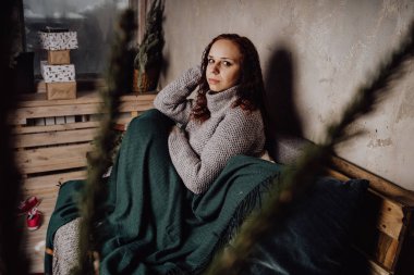 Bir genç kız yatakta oturmuş bir kazaklı bir battaniyeye huddled. Sıcak kazak giymiş kadın sokak stil giyim. Temiz cilt, uzun saç