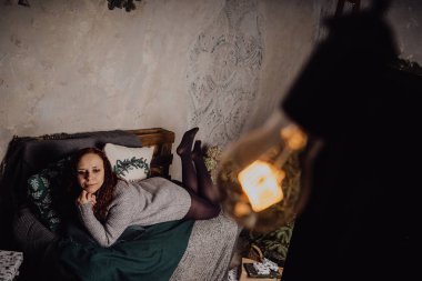 Kış konsepti. Bir gri örgü kazak sevimli genç kız. Güzel bir kadın beyaz bir yatak odasında rahatlatıcı bir şey. Elbise güzel kadınların sabah uyanıyor. Bir kazak giyen kadın