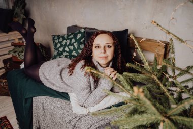 Kış konsepti. Bir gri örgü kazak sevimli genç kız. Güzel bir kadın beyaz bir yatak odasında rahatlatıcı bir şey. Elbise güzel kadınların sabah uyanıyor. Bir kazak giyen kadın