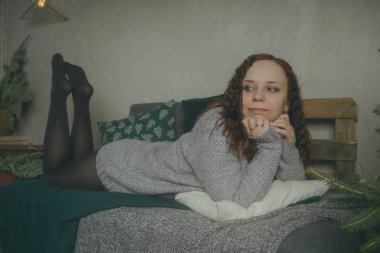 Kış konsepti. Bir gri örgü kazak sevimli genç kız. Güzel bir kadın beyaz bir yatak odasında rahatlatıcı bir şey. Elbise güzel kadınların sabah uyanıyor. Bir kazak giyen kadın