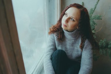 Genç bir kız bir kazaklı pencerenin önünde poz. Sıcak kazak giymiş kadın sokak stil giyim. Temiz cilt, uzun saç