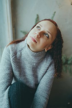 Genç bir kız bir kazaklı pencerenin önünde poz. Sıcak kazak giymiş kadın sokak stil giyim. Temiz cilt, uzun saç