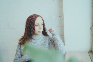 Genç bir kız bir kazaklı pencerenin önünde poz. Sıcak kazak giymiş kadın sokak stil giyim. Temiz cilt, uzun saç