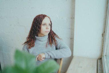 Genç bir kız bir kazaklı pencerenin önünde poz. Sıcak kazak giymiş kadın sokak stil giyim. Temiz cilt, uzun saç