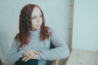 Genç bir kız bir kazaklı pencerenin önünde poz. Sıcak kazak giymiş kadın sokak stil giyim. Temiz cilt, uzun saç