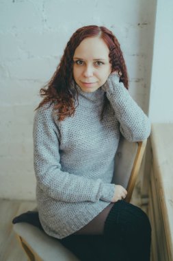 Genç bir kız bir kazaklı pencerenin önünde poz. Sıcak kazak giymiş kadın sokak stil giyim. Temiz cilt, uzun saç