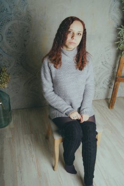 Gri bir duvara poz bir kazak bir genç kız. Sıcak kazak giymiş kadın sokak stil giyim. Temiz cilt, uzun saç