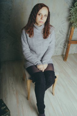 Gri bir duvara poz bir kazak bir genç kız. Sıcak kazak giymiş kadın sokak stil giyim. Temiz cilt, uzun saç