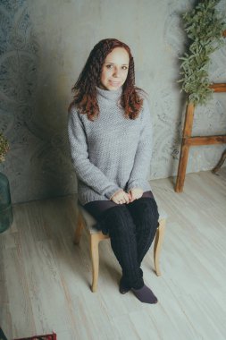 Gri bir duvara poz bir kazak bir genç kız. Sıcak kazak giymiş kadın sokak stil giyim. Temiz cilt, uzun saç