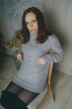 Gri bir duvara poz bir kazak bir genç kız. Sıcak kazak giymiş kadın sokak stil giyim. Temiz cilt, uzun saç