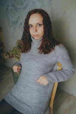 Gri bir duvara poz bir kazak bir genç kız. Sıcak kazak giymiş kadın sokak stil giyim. Temiz cilt, uzun saç