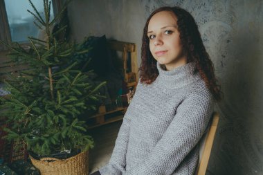 Gri bir duvara poz bir kazak bir genç kız. Sıcak kazak giymiş kadın sokak stil giyim. Temiz cilt, uzun saç