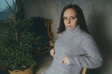 Gri bir duvara poz bir kazak bir genç kız. Sıcak kazak giymiş kadın sokak stil giyim. Temiz cilt, uzun saç