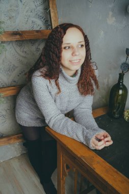 Gri bir duvara poz bir kazak bir genç kız. Sıcak kazak giymiş kadın sokak stil giyim. Temiz cilt, uzun saç