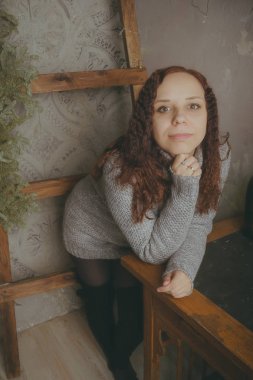 Gri bir duvara poz bir kazak bir genç kız. Sıcak kazak giymiş kadın sokak stil giyim. Temiz cilt, uzun saç