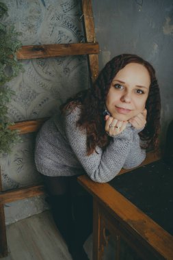 Gri bir duvara poz bir kazak bir genç kız. Sıcak kazak giymiş kadın sokak stil giyim. Temiz cilt, uzun saç