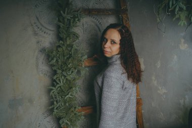 Gri bir duvara poz bir kazak bir genç kız. Sıcak kazak giymiş kadın sokak stil giyim. Temiz cilt, uzun saç