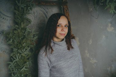 Gri bir duvara poz bir kazak bir genç kız. Sıcak kazak giymiş kadın sokak stil giyim. Temiz cilt, uzun saç