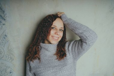 Gri bir duvara poz bir kazak bir genç kız. Sıcak kazak giymiş kadın sokak stil giyim. Temiz cilt, uzun saç