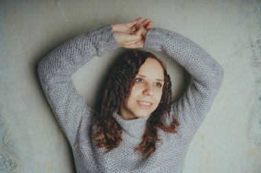 Gri bir duvara poz bir kazak bir genç kız. Sıcak kazak giymiş kadın sokak stil giyim. Temiz cilt, uzun saç