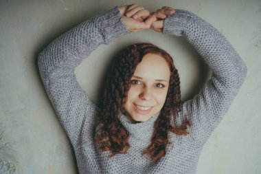 Gri bir duvara poz bir kazak bir genç kız. Sıcak kazak giymiş kadın sokak stil giyim. Temiz cilt, uzun saç