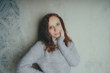 Gri bir duvara poz bir kazak bir genç kız. Sıcak kazak giymiş kadın sokak stil giyim. Temiz cilt, uzun saç