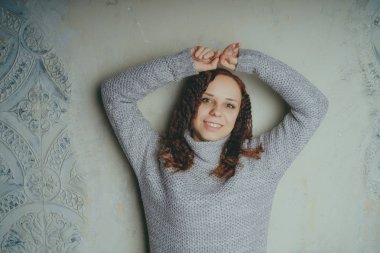 Gri bir duvara poz bir kazak bir genç kız. Sıcak kazak giymiş kadın sokak stil giyim. Temiz cilt, uzun saç