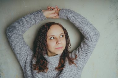 Gri bir duvara poz bir kazak bir genç kız. Sıcak kazak giymiş kadın sokak stil giyim. Temiz cilt, uzun saç