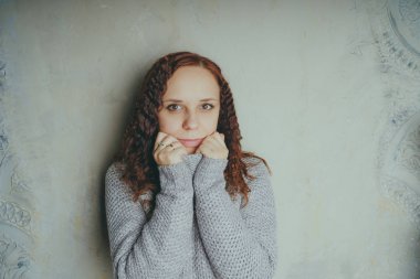 Gri bir duvara poz bir kazak bir genç kız. Sıcak kazak giymiş kadın sokak stil giyim. Temiz cilt, uzun saç