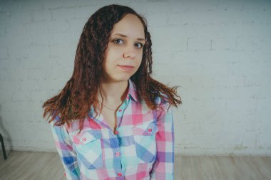 Deli kız beyaz bir duvar önünde poz. Sokak tarzı giyim: gömlek ve kot pantolon.