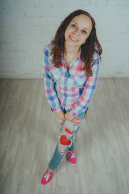 Deli kız beyaz bir duvar önünde poz. Sokak tarzı giyim: gömlek ve kot pantolon.