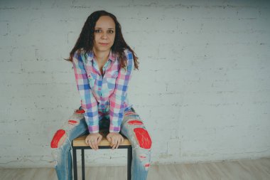 Deli kız beyaz bir duvar önünde poz. Sokak tarzı giyim: gömlek ve kot pantolon.