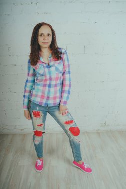 Deli kız beyaz bir duvar önünde poz. Sokak tarzı giyim: gömlek ve kot pantolon.