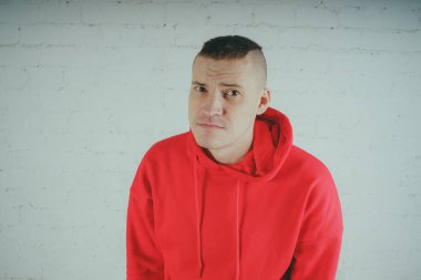 Yakışıklı olan bir tuğla duvar tarafından poz. Kırmızı kapüşonlu deli adam