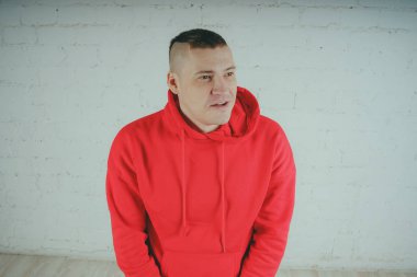 Yakışıklı olan bir tuğla duvar tarafından poz. Kırmızı kapüşonlu deli adam