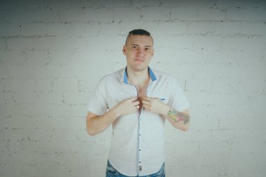 Duygusal ofis çalışanı dövmeli, beyaz duvara karşı bir sandalye üzerinde oturan adam. Bir kravat adam kot pantolon ve beyaz gömlek giymiş.