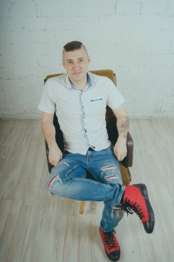 Duygusal ofis çalışanı dövmeli, beyaz duvara karşı bir sandalye üzerinde oturan adam. Bir kravat adam kot pantolon ve beyaz gömlek giymiş.