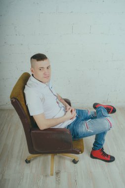 Duygusal ofis çalışanı dövmeli, beyaz duvara karşı bir sandalye üzerinde oturan adam. Bir kravat adam kot pantolon ve beyaz gömlek giymiş.